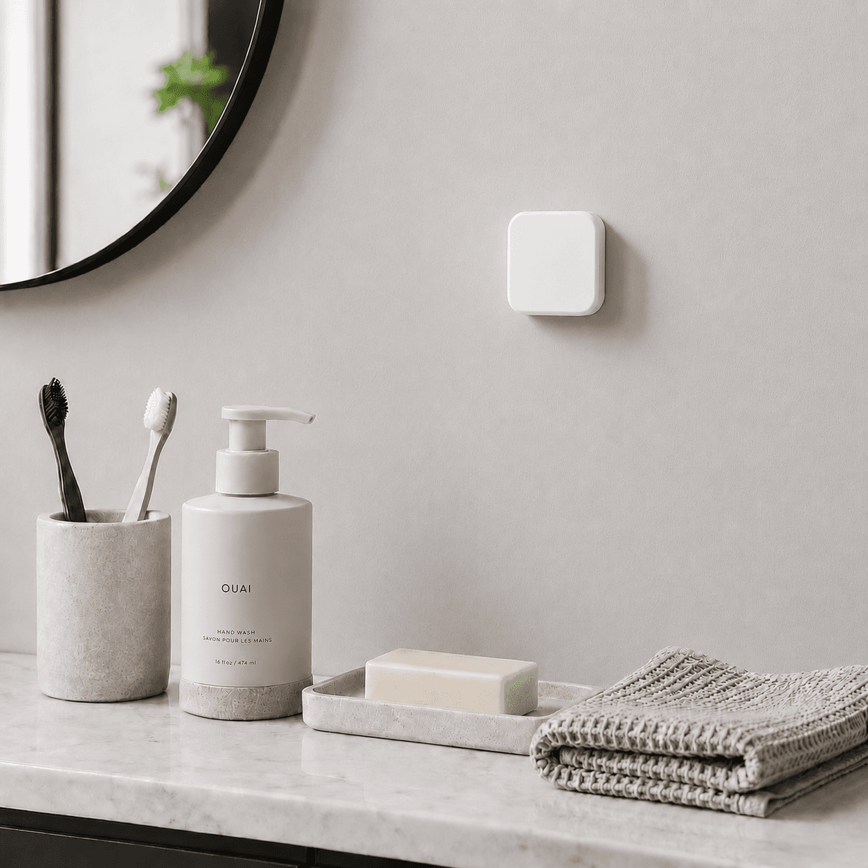 A white Slate block mounted on a bathroom wall above a counter with toothbrushes, hand wash, and a folded towel